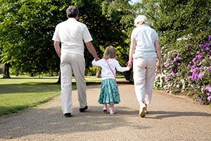 Grandparents Holding Hands And Walking With Grand-daughter In The Park.