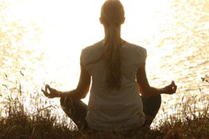Woman Facing Front, Mediating On A Meadow At Sunset.