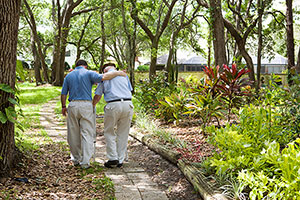 Male Caregiver Helping A Male Senior Walk In The Park.