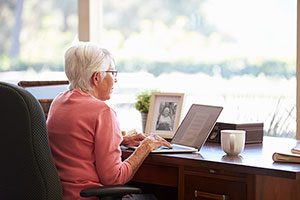 Senior Woman Dressed In Pink, Using Her Laptop On Her Desk At Home.