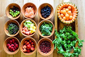 Heart-healthy Foods: 9 Bowls Of Grapes, Salmon, Berries, Spring Mix, Melons, Spinach, Pomegranate Arils Besides Kale And Cantaloupe Plates.