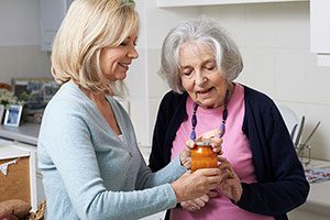 Occupational Therapist (OT) Helps Senior Woman Open Jar At Home.