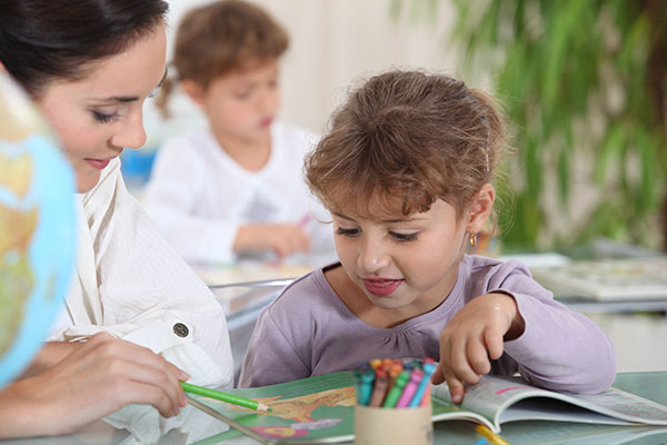 Speech language pathologist with little girl pointing at picture book.