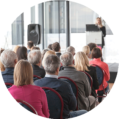 Woman giving presentation in a group wellness workshop to employees sitting in chairs, attentive.